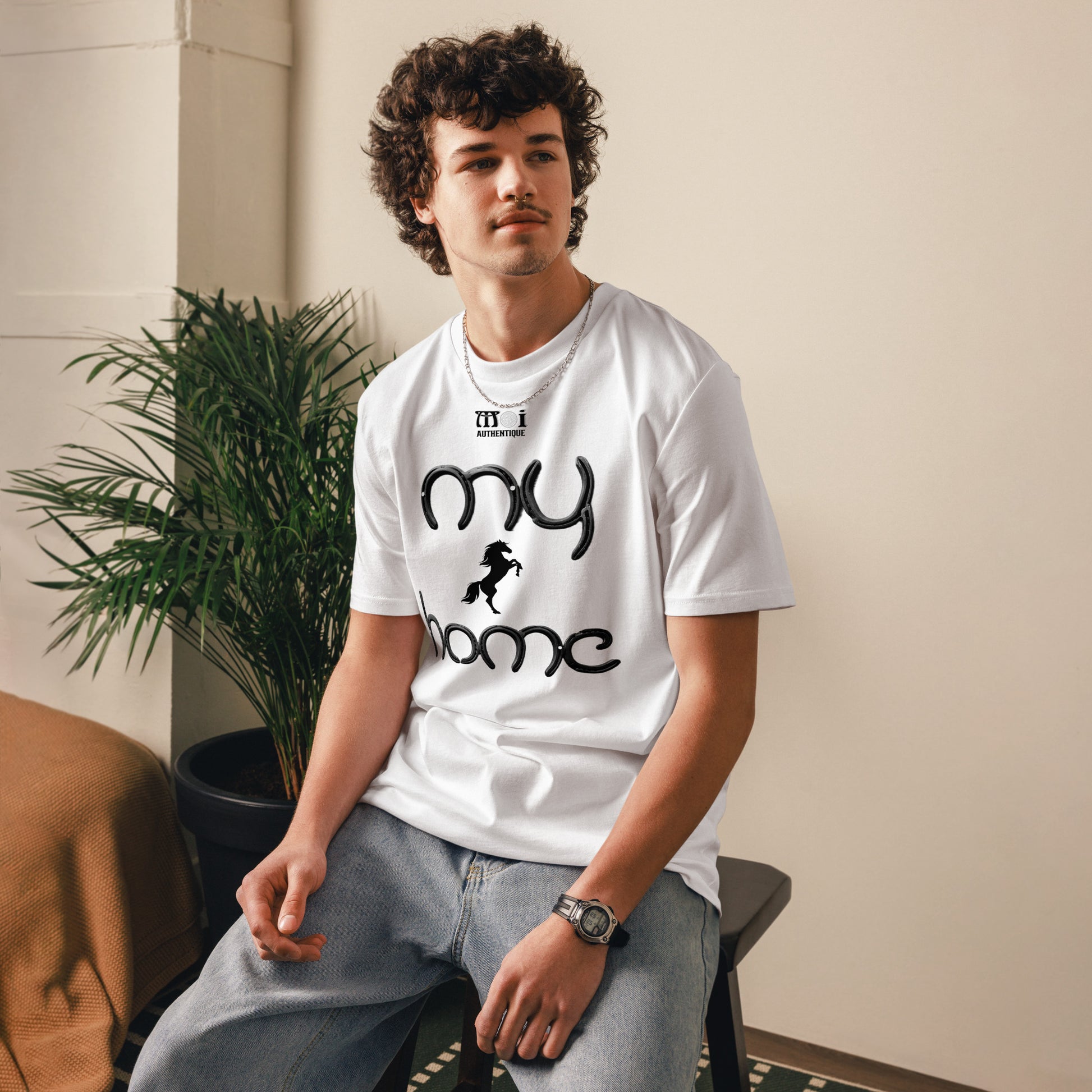 Man sitting on a stool wearing a white t-shirt with a small image of a horse with writing saying my home